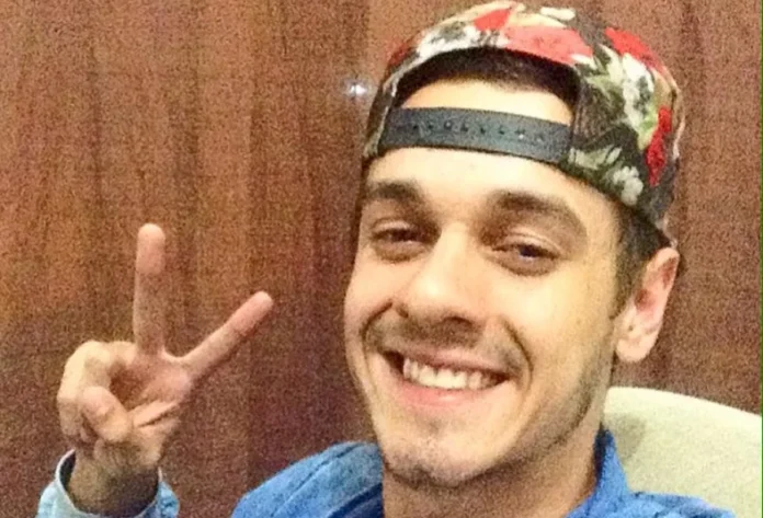 Identificado ciclista morto em acidente na BR-101 em Sombrio Fotografia de rosto de Marcos Vinicius Neumann Araujo Coelho, o ciclista de 28 anos que faleceu no acidente em Sombrio. Ele aparece sorrindo para a câmera, usando um boné estampado virado para trás e fazendo o sinal de paz com os dedos da mão direita.