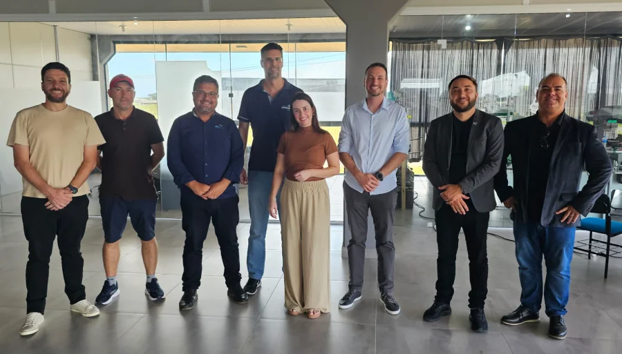 Oito representantes das cidades de Araranguá e Imbituba, incluindo o diretor Leandro José Müller e o vereador Samuca, posam para fotografia na sede da Aratec. O grupo, composto por sete homens e uma mulher, está posicionado lado a lado em um ambiente de escritório moderno com divisórias de vidro, simbolizando a cooperação técnica para o desenvolvimento tecnológico regional.