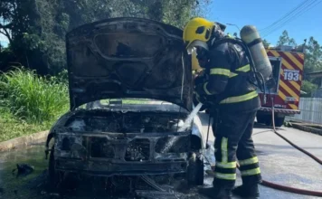 Incêndio destrói Saveiro em via pública de Criciúma Bombeiro realiza o resfriamento e a extinção de incêndio em um veículo utilitário no bairro Verdinho, em Criciúma. A imagem foca no combate direto às chamas que consumiram a parte frontal do automóvel.