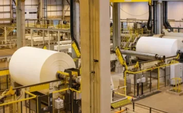 Juros altos travam crescimento da indústria em 2025 Vista interna de uma fábrica de papel com grandes rolos em produção e maquinário industrial. A imagem ilustra o setor produtivo brasileiro, que segundo a Confederação Nacional da Indústria (CNI) e dados do IBGE, enfrentou estagnação em 2025 devido aos altos juros da Taxa Selic e ao aumento das importações, resultando em um crescimento modesto de apenas 0,6% no ano.