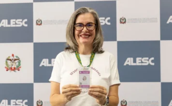Leis em SC garantem prioridade para quem tem fibromialgia Mulher com fibromialgia, Raquel Guesser exibe sua carteira de identificação, um marco da legislação catarinense que reconhece a condição como deficiência, durante evento na ALESC.