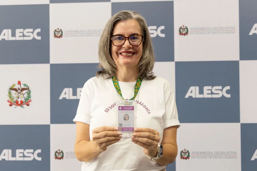 Mulher com fibromialgia, Raquel Guesser exibe sua carteira de identificação, um marco da legislação catarinense que reconhece a condição como deficiência, durante evento na ALESC.