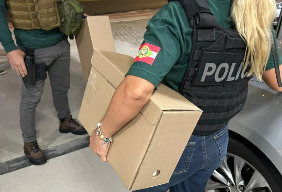 Policiais civis de Santa Catarina carregam caixas com documentos e materiais apreendidos durante a operação Control C, do GAECO, que investiga fraudes em licitações municipais no estado.