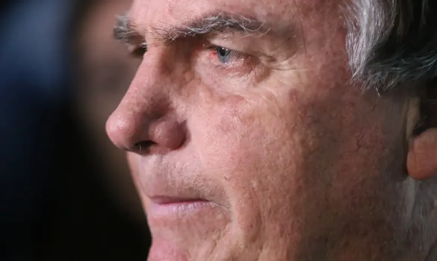 Foto em close e de perfil do ex-presidente Jair Bolsonaro, com expressão séria e olhar direcionado ao horizonte. A imagem é utilizada para ilustrar a notícia sobre o laudo médico da Polícia Federal que aponta alterações neurológicas em seu quadro de saúde no Complexo da Papuda.