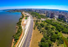 PIB do RS deve crescer 4,6% e liderar expansão nacional Vista aérea panorâmica da cidade de Porto Alegre, capital do Rio Grande do Sul, mostrando a orla urbanizada do Lago Guaíba, avenidas movimentadas com veículos e a densidade de prédios ao fundo. A imagem ilustra o principal centro urbano do estado, que lidera a expansão econômica nacional em 2026, impulsionada pela agropecuária e com reflexos nos setores de indústria e serviços.
