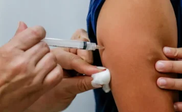 Primeiro caso de mpox em 2026 é confirmado no RS Imagem focada no momento da imunização, mostrando a aplicação de uma dose de vacina em ambiente clínico. O fundo é neutro e o foco está no procedimento médico.