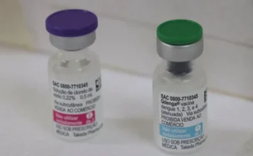 RS amplia vacina contra dengue para todos os municípios Fotografia em close-up de dois frascos da vacina Qdenga sobre uma superfície clara. O frasco à esquerda possui tampa roxa e o da direita possui tampa verde, com o rótulo exibindo o nome do imunizante utilizado na campanha contra a dengue para crianças e adolescentes.