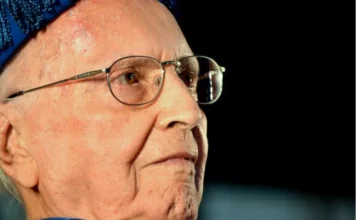 Ruy Hülse: 100 anos do visionário que fundou a Unesc Retrato em close de perfil do ex-prefeito Ruy Hülse, fundador da Unesc, um senhor idoso de óculos, vestindo trajes acadêmicos em tons de azul. Ele possui uma expressão serena e o olhar voltado para o horizonte, simbolizando seu legado centenário.