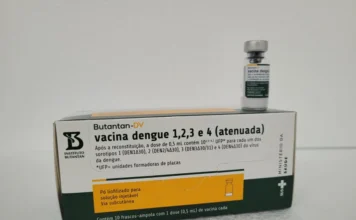 SC inicia vacinação contra dengue para profissionais da saúde A imagem apresenta, em destaque central, uma caixa de cor branca e laranja do imunizante Butantan-DV, a vacina contra a dengue produzida pelo Instituto Butantan. Na embalagem, lê-se o texto "vacina dengue 1, 2, 3 e 4 (atenuada)", indicando a proteção contra os quatro sorotipos da doença. Sobre a caixa, encontra-se um pequeno frasco-ampola de vidro com o selo do fabricante. No canto inferior direito da caixa, estão visíveis as logomarcas do Ministério da Saúde e do SUS.