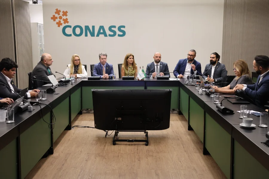 Fotografia em plano médio de uma sala de reuniões no Conass, em Brasília. Ao centro, uma mesa em formato de 