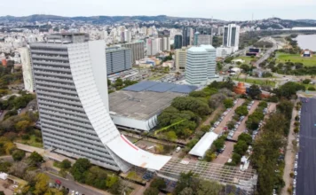 SES alerta para fim de adesão ao Geração Consciente 2026 no RS Vista aérea do Centro Administrativo Fernando Ferrari (CAFF), em Porto Alegre, onde está sediada a Secretaria da Saúde do Rio Grande do Sul. O prédio, com sua icônica fachada branca e curva, aparece em destaque sob um céu claro, cercado por vegetação e outras edificações governamentais. A imagem simboliza a gestão estadual responsável pela coordenação do programa Geração Consciente.