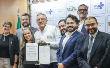 SUS terá exame de DNA que reduz diagnóstico para seis meses Uma foto de grupo com nove pessoas em um evento oficial. No centro, o Ministro da Saúde, Dr. Alexandre Padilha, e uma mulher seguram e exibem um documento oficial em uma pasta preta. O documento possui o título 'HABILITAÇÃO DE NOVOS SERVIÇOS PARA TRATAMENTO DE DOENÇAS RARAS' e menciona a 'POLÍTICA NACIONAL DE ATENÇÃO INTEGRAL ÀS PESSOAS COM DOENÇAS RARAS', com logomarcas do SUS e do Governo Federal. O Dr. Padilha veste um casaco branco com seu nome e cargo bordados. As outras sete pessoas, homens e mulheres, estão ao redor, sorrindo e olhando para a câmera. O fundo é um painel modular com repetições dos logos 'SUS 30 ANOS', 'MINISTÉRIO DA SAÚDE' e 'GOVERNO FEDERAL BRASIL', ao lado de uma bandeira do Brasil à esquerda.