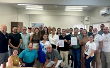 Santa Rosa do Sul recebe R$ 2,4 mi para habitação e social Prefeito de Santa Rosa do Sul, Almides Roberg da Rosa, e a Secretária de Estado da Assistência Social, Adeliana Dal Pont, seguram os convênios assinados para a construção de casas populares e uma residência de acolhimento, cercados por um grupo de autoridades locais e membros da comunidade no auditório municipal. A imagem marca a liberação de R$ 2,4 milhões em recursos estaduais para o município.