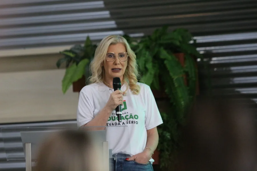 Luciane Bisognin Ceretta, secretária de Estado da Educação e reitora licenciada da Unesc, fala ao microfone durante palestra sobre a importância da graduação e o mercado de trabalho no campus da Unesc Araranguá. Ela veste uma camiseta branca com a frase 