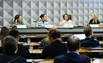 Senado discute prevenção à violência infantil no Carnaval Fotografia da audiência pública na Comissão de Direitos Humanos (CDH) do Senado mencionada na matéria. Na mesa principal, a senadora Damares Alves gesticula com as mãos enquanto fala, sentada entre Luciana Temer e a Coronel Ana Paula Barros Habka à sua direita, e Lais Cardoso Peretto à sua esquerda. Uma plateia assiste em primeiro plano. A imagem ilustra o debate sobre a proteção de crianças e adolescentes no Carnaval.