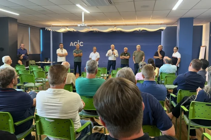 Setor do arroz avalia medidas do Governo contra a crise Homens reunidos em uma sala de conferências da ACIC durante a reunião da Câmara Setorial da Cadeia Produtiva do Arroz. Ao fundo, autoridades e representantes do setor, incluindo o deputado José Milton Scheffer e Walmir Rampinelli, estão de pé diante de uma plateia sentada em cadeiras verdes, discutindo propostas para o setor orizícola catarinense.