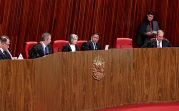 TSE mantém mandato de Jorge Seif por unanimidade Vista geral do Plenário do Tribunal Superior Eleitoral (TSE) durante sessão de julgamento. Os ministros, vestindo togas pretas, estão sentados atrás de uma longa bancada de madeira curva com o brasão da República ao centro, onde decidiram, por unanimidade, manter o mandato do senador Jorge Seif.