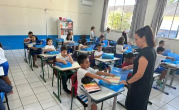 Timbé do Sul inicia ano letivo com entrega de kits escolares Alunos da EMEF Frei Modesto recebem materiais escolares no primeiro dia de aula. A imagem mostra as crianças entusiasmadas manuseando os kits sobre as mesas enquanto a professora orienta a atividade.