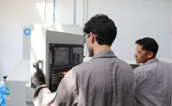Unesc abre matrículas para Engenharias e Tecnologia Dois estudantes dos cursos de Engenharia e Tecnologia da Unesc, usando óculos de proteção e macacões cinza, operam uma máquina industrial com painel de controle digital em um laboratório da universidade, ilustrando a formação prática oferecida.