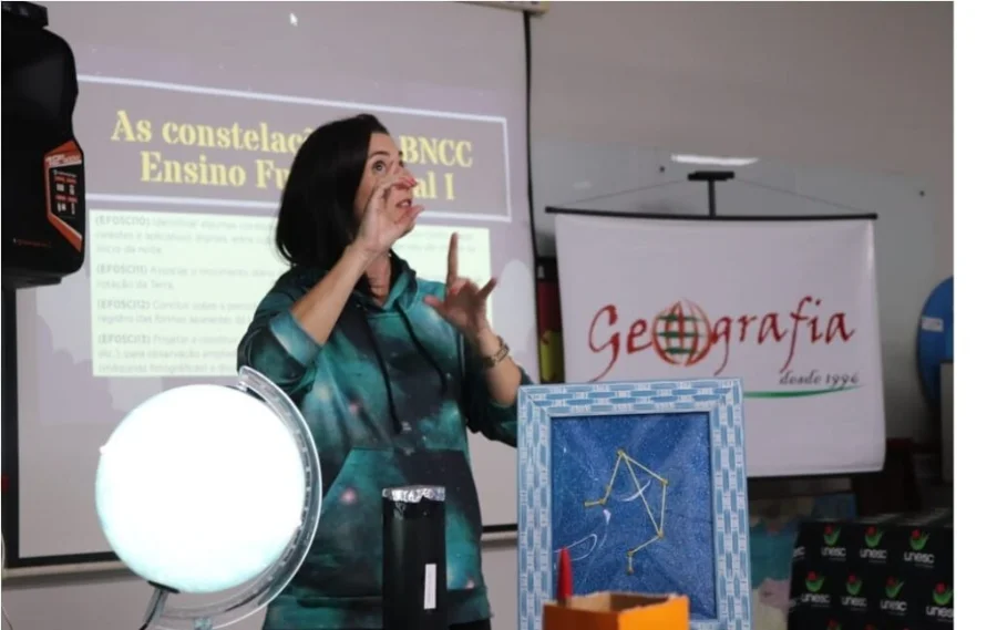 Unesc abre matrículas para licenciaturas com bolsas de 100% Imagem demonstrativa de uma aula prática de Licenciatura na Unesc. Uma docente utiliza modelos de constelações e um globo terrestre para ensinar Geografia, ilustrando a metodologia de ensino dinâmica dos cursos que estão com bolsas de estudo de 100% disponíveis.