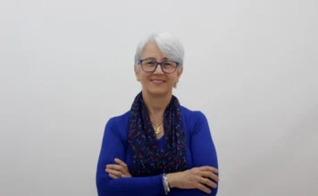 Unesc celebra Dia das Mulheres e Meninas na Ciência Uma mulher de cabelos grisalhos curtos e óculos de armação azul, vestindo uma blusa azul de manga longa e um lenço estampado em tons de azul e vermelho, sorri com os braços cruzados. Ela representa uma das pesquisadoras da Unesc destacadas na matéria sobre o Dia Internacional das Mulheres e Meninas na Ciência.