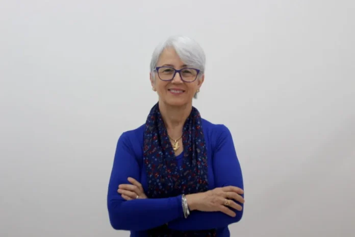 Unesc celebra Dia das Mulheres e Meninas na Ciência Uma mulher de cabelos grisalhos curtos e óculos de armação azul, vestindo uma blusa azul de manga longa e um lenço estampado em tons de azul e vermelho, sorri com os braços cruzados. Ela representa uma das pesquisadoras da Unesc destacadas na matéria sobre o Dia Internacional das Mulheres e Meninas na Ciência.