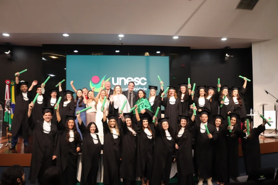 Unesc forma novos psicólogos em cerimônia especial Formandos e autoridades celebram no palco do Auditório Ruy Hülse após a Colação de Grau Especial do curso de Psicologia da Unesc, com os novos profissionais levantando seus diplomas.