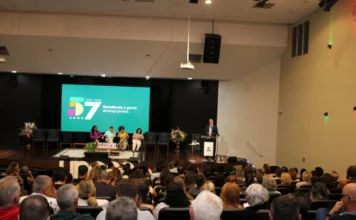 Unesc inicia Formação de Docentes 2026 com foco em empatia Vista panorâmica do auditório Ruy Hülse lotado de professores durante a abertura da Formação Permanente de Docentes 2026 da Unesc. No palco, o palestrante Paulo Roberto de Andrada Pacheco fala ao púlpito, posicionado à direita. Ao fundo, um telão digital exibe a identidade visual dos 57 anos da Unesc com a frase "Excelência a gente alcança juntos" e a inscrição "Universidade Comunitária". À esquerda, quatro integrantes da reitoria acompanham a apresentação sentados em poltronas.