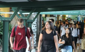 Unesc inicia letivo 2026 com foco em diversidade e inclusão Estudantes de diversos perfis caminham pelo Espaço Cultural "Toque de Arte" no campus da Unesc, em Criciúma. No centro da imagem, uma jovem sorri enquanto transita pelo local, representando a movimentação e o clima de acolhimento no primeiro dia de aulas do semestre letivo de 2026.