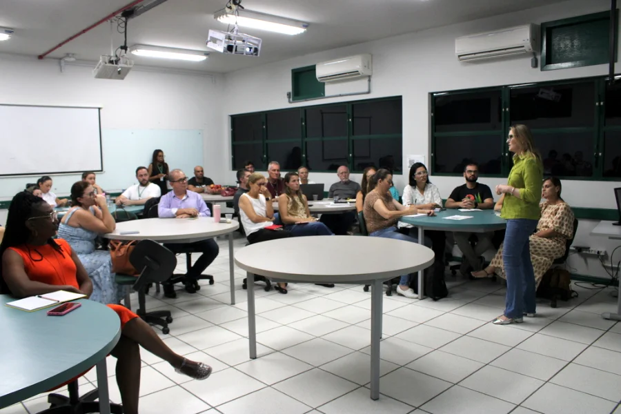 Mulher ministra palestra para grupo de professores em sala de aula, ilustrando atividade do Programa de Formação Docente da Unesc.