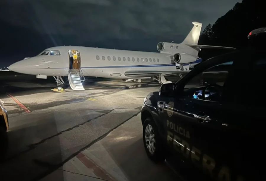 Jato executivo estacionado em pista de pouso durante a noite sob vigilância. A imagem remete ao universo das aeronaves de alto valor, como o modelo de Daniel Vorcaro citado no texto.