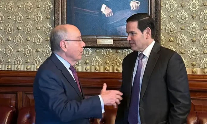 Vieira e Rubio alinham visita de Lula aos EUA em março Fotografia em plano médio do Ministro das Relações Exteriores, Mauro Vieira, e do Secretário de Estado dos EUA, Marco Rubio. Vieira, à esquerda, gesticula enquanto fala, e Rubio, à direita, escuta atentamente. Ambos vestem ternos escuros e gravatas em tons de vinho e roxo. Eles estão em uma sala de reuniões formal com papel de parede ornamentado e uma pintura clássica ao fundo.