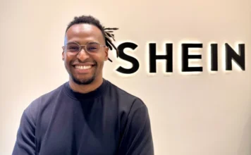 ACIVA promove palestra sobre vendas no marketplace da SHEIN Thiago Farhat, gerente de parcerias da SHEIN Marketplace no Brasil, sorridente em frente ao logotipo iluminado da SHEIN. Imagem focada no palestrante que abordará estratégias de vendas e e-commerce para empresários de Araranguá.