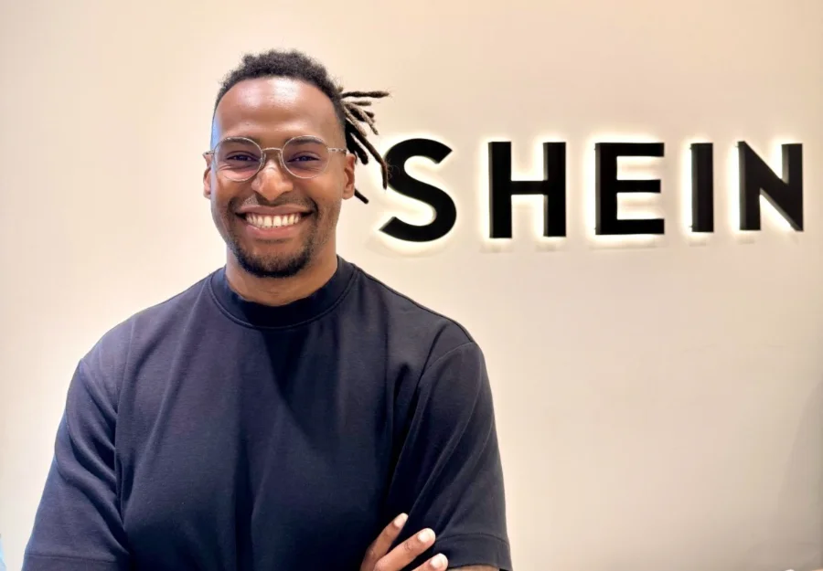 Thiago Farhat, gerente de parcerias da SHEIN Marketplace no Brasil, sorridente em frente ao logotipo iluminado da SHEIN. Imagem focada no palestrante que abordará estratégias de vendas e e-commerce para empresários de Araranguá.