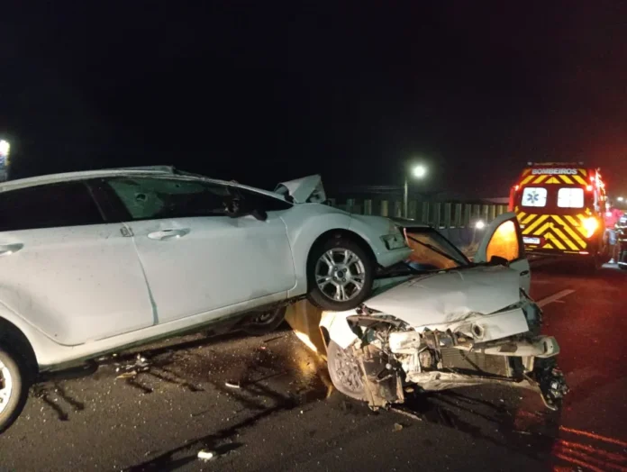Acidente na BR-101 deixa adolescente ferida em Sombrio Acidente de trânsito na BR-101 em Sombrio mostra um carro branco sobre o outro após colisão noturna. Ao fundo, ambulância do Corpo de Bombeiros com luzes acesas realiza o atendimento da ocorrência no bairro Januária.