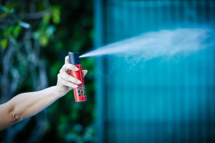 Alesc aprova spray de pimenta para mulheres sob proteção Mão feminina segurando e acionando um frasco de spray de pimenta vermelho e preto, expelindo gás. Uma representação do dispositivo de defesa pessoal que será fornecido a mulheres sob medida protetiva em Santa Catarina após aprovação da Alesc.
