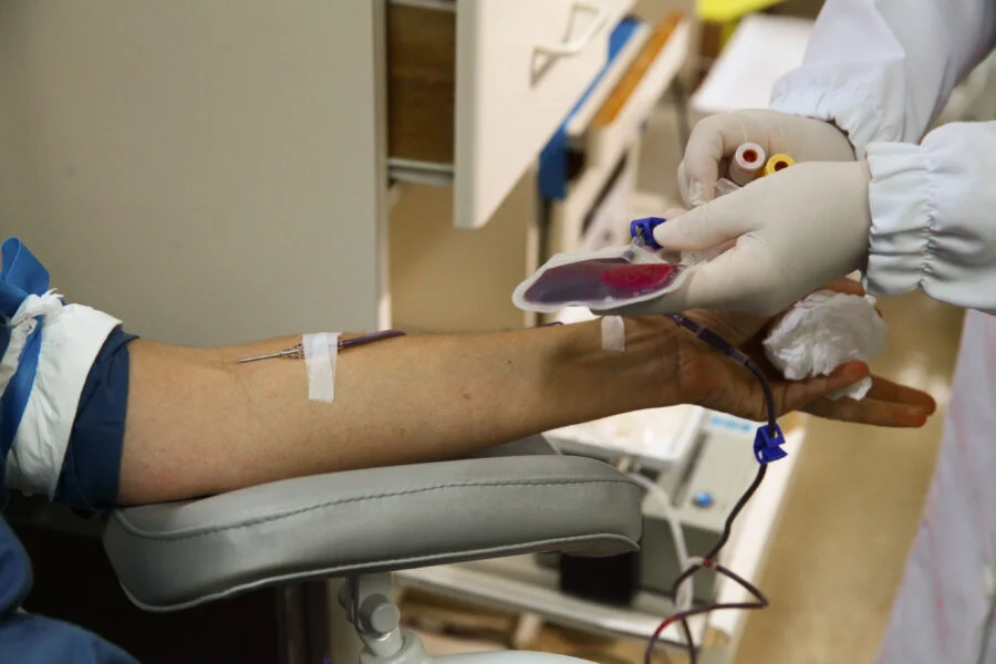 Alesc inicia análise de novos projetos de lei em SC Foto em close-up do braço de um doador em procedimento de doação de sangue em Santa Catarina, com agulha e bolsa de coleta visíveis. Imagem ilustra o projeto de lei da Alesc (PL 153/2026) sobre incentivos fiscais para doadores regulares de sangue.
