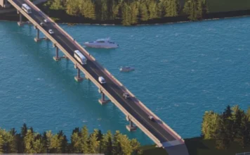 Araranguá: Licitação da 4ª ponte recebe menor lance Projeção digital em 3D apresenta a perspectiva artística da futura quarta ponte de Araranguá. A imagem mostra uma longa estrutura de concreto atravessando um rio azul, com veículos como ônibus e carros circulando sobre ela. Na água, há embarcações próximas aos pilares e, nas margens, uma densa vegetação de árvores verdes completa o cenário.