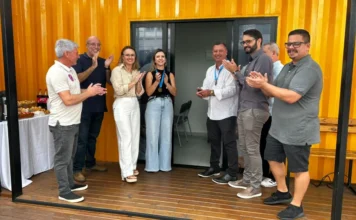 Araranguá inaugura nova Sala do Empreendedor na Praça Autoridades e representantes de entidades de classe durante a inauguração da nova Sala do Empreendedor de Araranguá, instalada em uma estrutura amarela na Praça Hercílio Luz. O grupo aparece sorrindo e aplaudindo em frente à entrada do novo espaço de apoio ao empreendedorismo local.