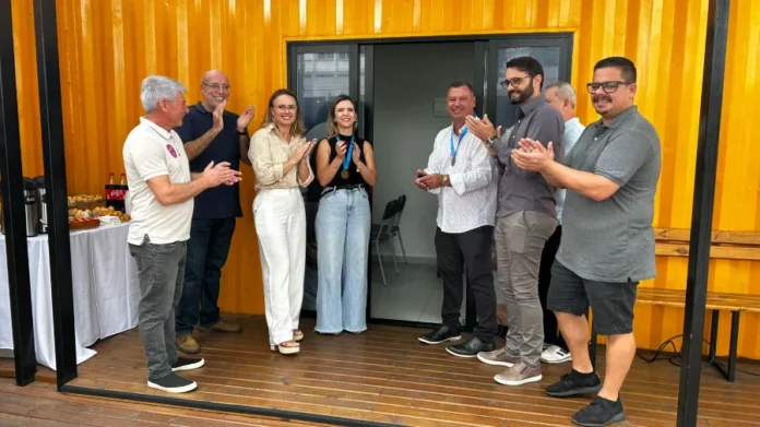 Araranguá inaugura nova Sala do Empreendedor na Praça Autoridades e representantes de entidades de classe durante a inauguração da nova Sala do Empreendedor de Araranguá, instalada em uma estrutura amarela na Praça Hercílio Luz. O grupo aparece sorrindo e aplaudindo em frente à entrada do novo espaço de apoio ao empreendedorismo local.