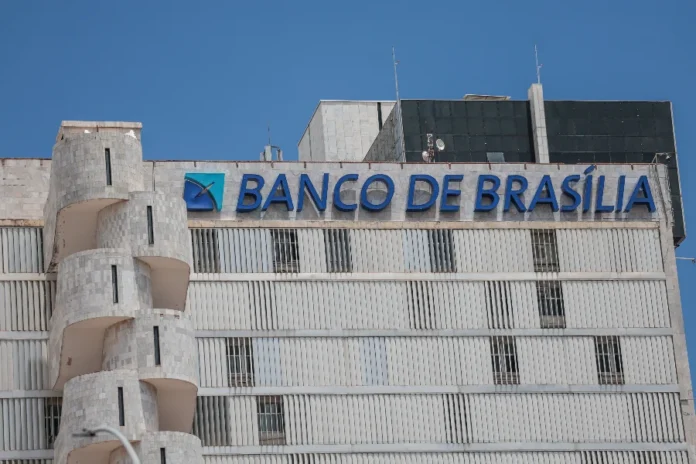 BRB presidente descarta privatização e defende socorro Fachada de um edifício de arquitetura moderna em tons claros, destacando no topo o letreiro com o nome "BANCO DE BRASÍLIA" em letras azuis. A imagem ilustra a sede da instituição que atualmente discute medidas de recomposição de capital e descarta processos de privatização.
