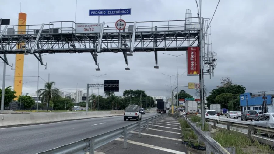 Pórtico metálico de sistema de pedágio free-flow instalado sobre rodovia com sensores de cobrança eletrônica e placa indicativa de livre passagem em dia nublado.