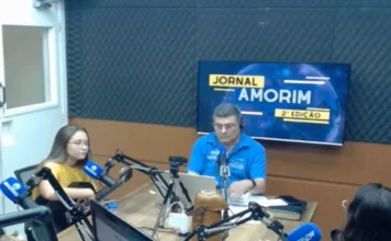 Cantora Thalyta Silva fala sobre chamado e fé Cantora gospel Thalyta Silva segura um violão durante entrevista nos estúdios da Rádio 102.9 Amorim FM. Ao fundo, monitor exibe a identidade visual do Jornal Amorim 2ª Edição em um ambiente de estúdio profissional.