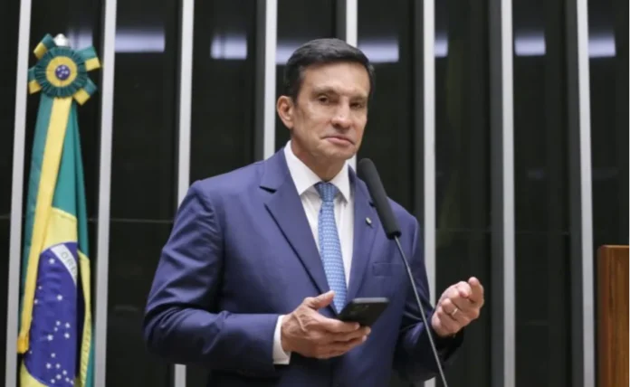 Comissão aprova rastreamento digital contra garimpo ilegal O deputado federal Sidney Leite (PSD-AM) fala no púlpito da Câmara dos Deputados sobre o projeto de rastreabilidade digital do ouro. Ele segura um smartphone e está de terno azul. No fundo, painéis de votação e bandeira do Brasil.