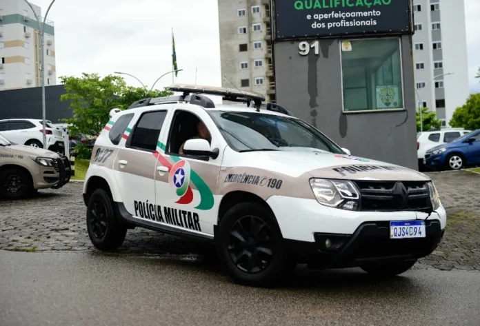 Crianças são resgatadas em local de tráfico em Criciúma Viatura Renault Duster da Polícia Militar de Santa Catarina (PMSC) estacionada em frente a um prédio de qualificação profissional em dia nublado. A foto, em close-up, mostra o fardamento do policial dentro do veículo, o logotipo da PMSC, a identificação de emergência 190 e a placa QJS4C94. Imagem ilustrativa para notícias sobre ações policiais, segurança pública e combate ao tráfico de drogas em SC, incluindo Criciúma.