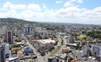 Criciúma é vice-líder em ensino técnico em Santa Catarina Vista aérea panorâmica da área urbana de Criciúma, em Santa Catarina, exibindo densidade de edifícios residenciais e comerciais, avenidas movimentadas com veículos e vegetação ao fundo sob um céu claro com nuvens. A imagem ilustra o desenvolvimento e a infraestrutura do município mencionado no Ranking de Competitividade.