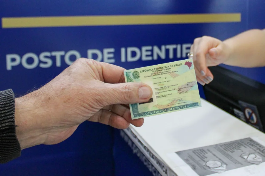 Pessoa segura nova Carteira de Identidade em frente ao balcão de atendimento do Posto de Identificação (Pedic) em Criciúma, Santa Catarina.