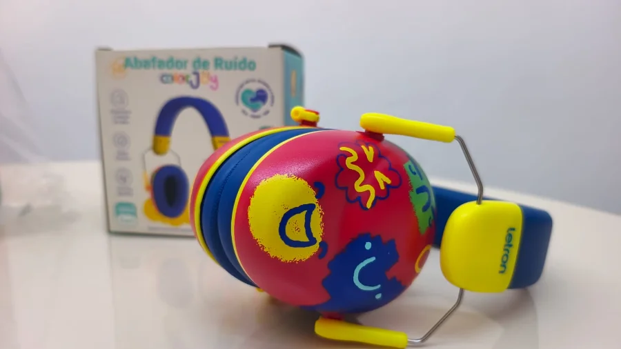 Criciúma entrega 500 abafadores de ruído para escolas Fotografia em close-up de um abafador de ruído infantil com design colorido em tons de vermelho, azul e amarelo, decorado com desenhos lúdicos. Ao fundo, em desfoque, aparece a embalagem do produto. O equipamento é um dos 500 dispositivos distribuídos pelo Governo de Criciúma para apoiar a inclusão de estudantes com hipersensibilidade auditiva na rede municipal de ensino.