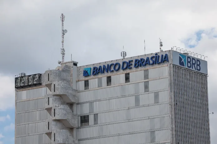 DF aprova aporte de R$ 6,6 bi no BRB para cobrir rombo Imagem da fachada lateral de um edifício de cor cinza onde se lê, no topo, o letreiro "BANCO DE BRASÍLIA" ao lado da logomarca e da sigla BRB. A foto, tirada sob um céu nublado, identifica a sede da instituição financeira que recebeu autorização da Câmara Legislativa do Distrito Federal para um aporte de até R$ 6,6 bilhões para cobrir prejuízos financeiros.