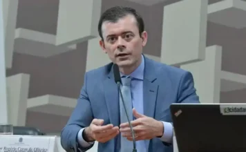 Dario Durigan define nova cúpula do Ministério da Fazenda Rogério Ceron, novo secretário-executivo do Ministério da Fazenda, de terno azul, gesticulando enquanto fala ao microfone em uma sessão oficial em Brasília.